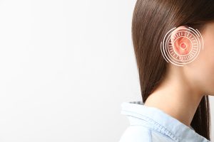 Young woman with hearing aid on light background